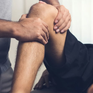 Therapist treating injured knee of athlete male patient