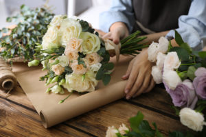Florist,Wrapping,Beautiful,Wedding,Bouquet,With,Paper,At,Wooden,Table,